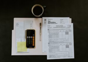 A person sorts receipts and tax documents at a kitchen table with a laptop and calculator.