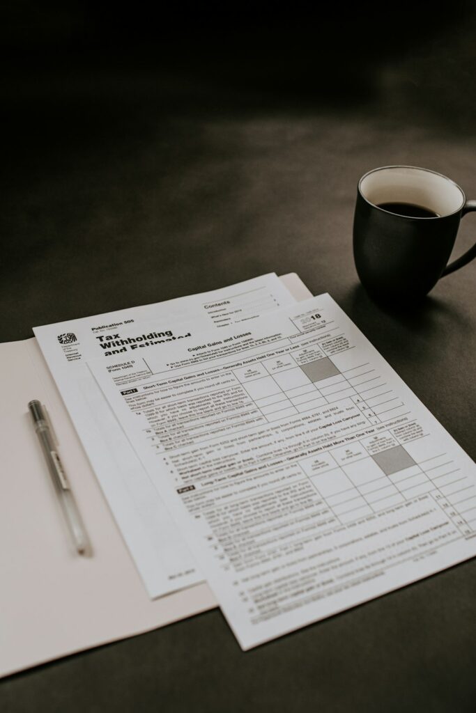 A person sits at a kitchen table reviewing tax documents and receipts with a calculator and laptop.