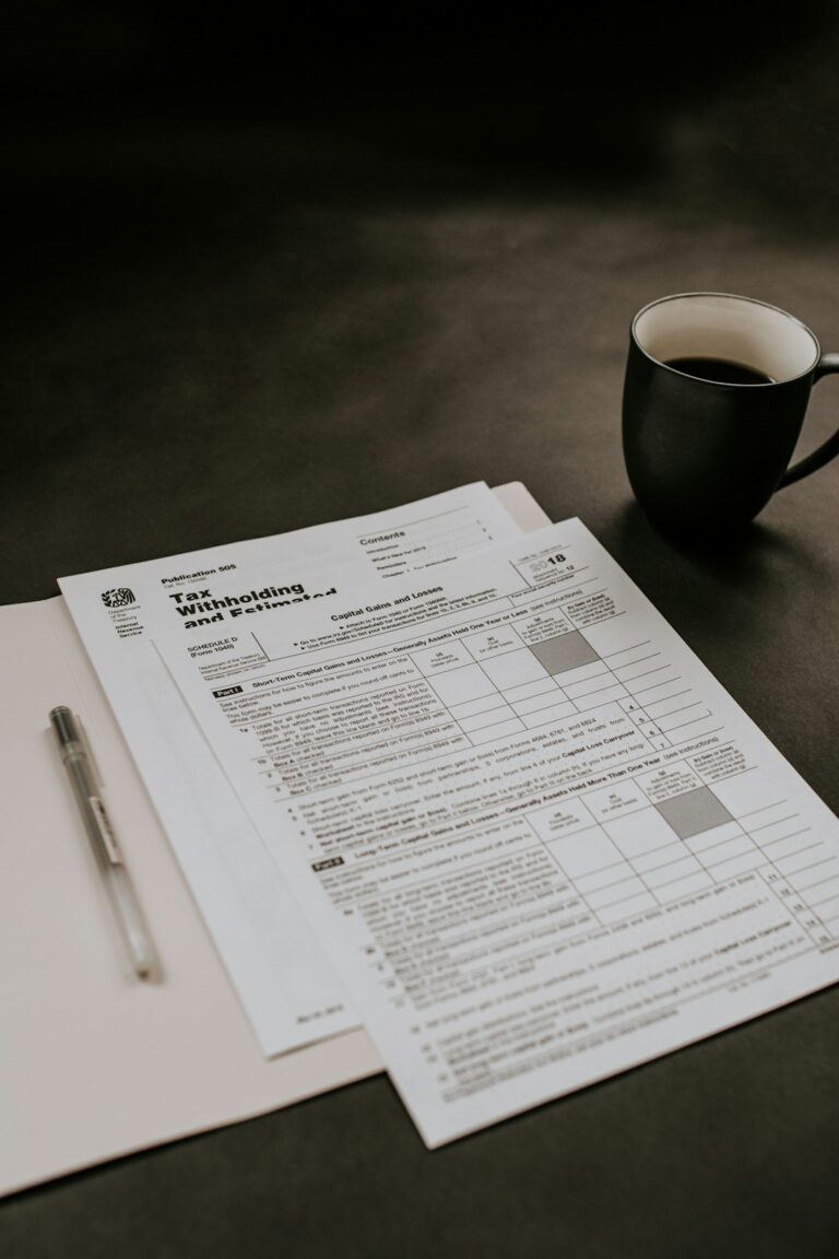A person sits at a kitchen table reviewing tax documents and receipts with a calculator and laptop.