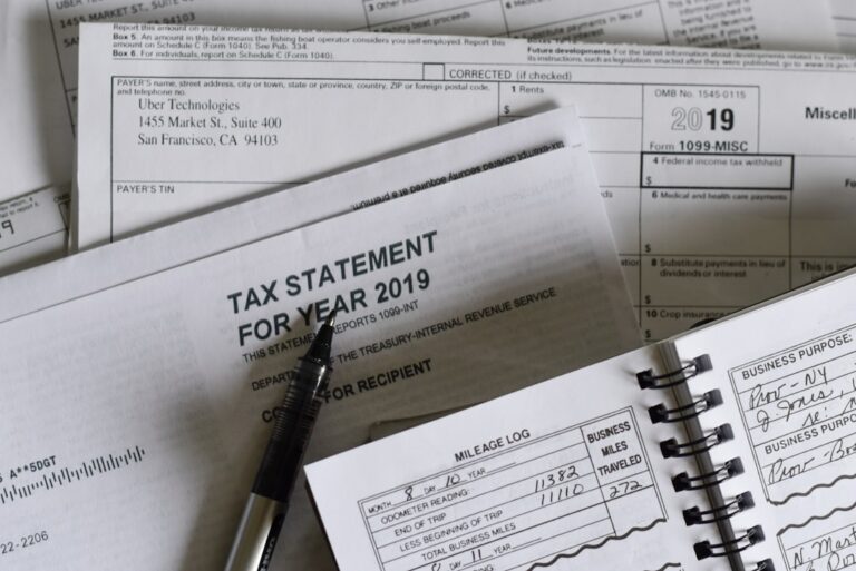 People organizing tax documents and pay stubs at their kitchen table with a laptop and calculator.